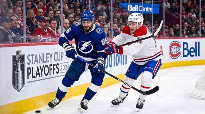 Dynamic on-ice action photo from Game 4 of the 2026 Stanley Cup Playoffs, showing Tampa Bay Lightning forward Nikita Kucherov (#86, blue jersey) battling Montreal Canadiens defenseman Lane Hutson (#?, white jersey) for puck possession near the boards in a packed Bell Centre.