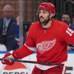 A conceptual image showing New York Rangers center Vincent Trocheck wearing a Detroit Red Wings home jersey #16 on the ice, illustrating NHL trade rumors.