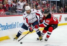 Washington Capitals captain Alex Ovechkin in an away white jersey battles New Jersey Devils star Jack Hughes for the puck during an NHL game.