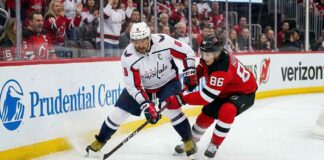 Washington Capitals captain Alex Ovechkin in an away white jersey battles New Jersey Devils star Jack Hughes for the puck during an NHL game.