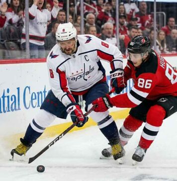Washington Capitals captain Alex Ovechkin in an away white jersey battles New Jersey Devils star Jack Hughes for the puck during an NHL game.