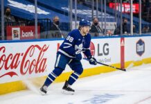 William Nylander (#88) of the Toronto Maple Leafs, in dynamic action on the ice, skating along the arena boards with visible advertising for Coca-Cola and LG, during an NHL game.