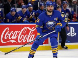 Alex Tuch Contract Extension Updates: Sabres Free Agency Rumors Buffalo Sabres forward Alex Tuch in action on the ice, skating past Coca-Cola and PS5 rink board advertisements during an NHL game.