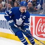 Toronto Maple Leafs captain Auston Matthews controls the puck during an NHL game against a background with Coca-Cola advertising.