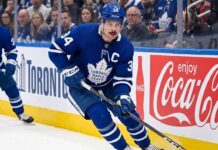 Toronto Maple Leafs captain Auston Matthews controls the puck during an NHL game against a background with Coca-Cola advertising.