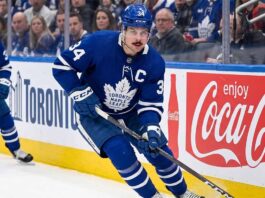 Toronto Maple Leafs captain Auston Matthews controls the puck during an NHL game against a background with Coca-Cola advertising.