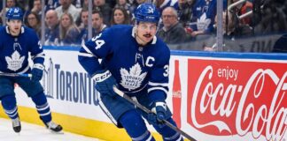 Toronto Maple Leafs captain Auston Matthews controls the puck during an NHL game against a background with Coca-Cola advertising.