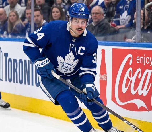 Toronto Maple Leafs captain Auston Matthews controls the puck during an NHL game against a background with Coca-Cola advertising.