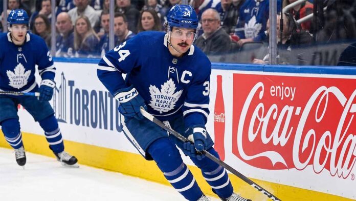 Toronto Maple Leafs captain Auston Matthews controls the puck during an NHL game against a background with Coca-Cola advertising.