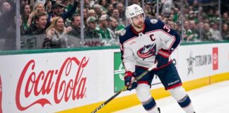 Columbus Blue Jackets captain Boone Jenner (38) in a white away jersey looking focused on the ice while handling the puck.