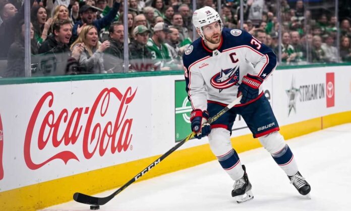 boone-jenner-columbus-blue-jackets-captain Columbus Blue Jackets captain Boone Jenner (38) in a white away jersey looking focused on the ice while handling the puck.