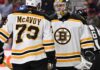 Charlie McAvoy (left, #73) of the Boston Bruins and goalie Linus Ullmark in away jerseys sharing a conversation on the ice during an NHL hockey game.
