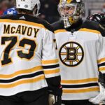 Charlie McAvoy (left, #73) of the Boston Bruins and goalie Linus Ullmark in away jerseys sharing a conversation on the ice during an NHL hockey game.