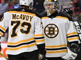 Charlie McAvoy (left, #73) of the Boston Bruins and goalie Linus Ullmark in away jerseys sharing a conversation on the ice during an NHL hockey game.