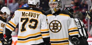 Charlie McAvoy (left, #73) of the Boston Bruins and goalie Linus Ullmark in away jerseys sharing a conversation on the ice during an NHL hockey game.
