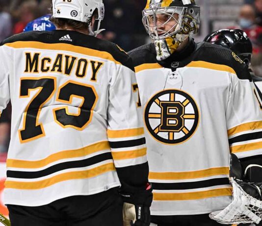 Charlie McAvoy (left, #73) of the Boston Bruins and goalie Linus Ullmark in away jerseys sharing a conversation on the ice during an NHL hockey game.