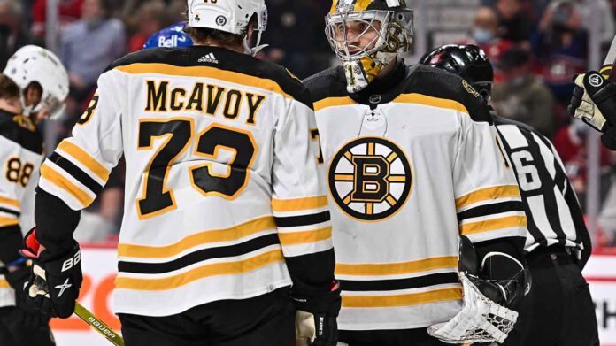 Charlie McAvoy (left, #73) of the Boston Bruins and goalie Linus Ullmark in away jerseys sharing a conversation on the ice during an NHL hockey game.