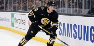 Boston Bruins defenseman Mason Lohrei looks to advance the puck during a game. Lohrei, wearing jersey number 6, is the subject of recent NHL trade rumors suggesting he could be moved for a top-six forward.