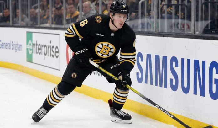 Boston Bruins defenseman Mason Lohrei looks to advance the puck during a game. Lohrei, wearing jersey number 6, is the subject of recent NHL trade rumors suggesting he could be moved for a top-six forward.