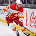 Calgary Flames Offseason Rebuild: Who Stays and Who Goes? Calgary Flames alternate captain Jonathan Huberdeau skating along the boards with the puck during an NHL game, next to a Coca-Cola advertisement.