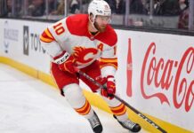 Calgary Flames alternate captain Jonathan Huberdeau skating along the boards with the puck during an NHL game, next to a Coca-Cola advertisement.