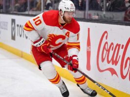 Calgary Flames Offseason Rebuild: Who Stays and Who Goes? Calgary Flames alternate captain Jonathan Huberdeau skating along the boards with the puck during an NHL game, next to a Coca-Cola advertisement.
