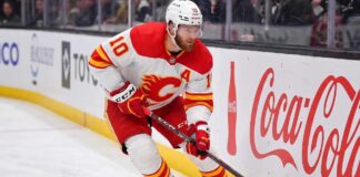 Calgary Flames alternate captain Jonathan Huberdeau skating along the boards with the puck during an NHL game, next to a Coca-Cola advertisement.