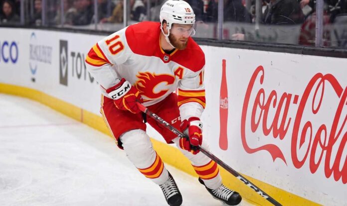 calgary-flames-offseason-rebuild-rumors Calgary Flames alternate captain Jonathan Huberdeau skating along the boards with the puck during an NHL game, next to a Coca-Cola advertisement.