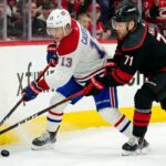How to Watch Montreal Canadiens vs Carolina Hurricanes Game 2 on TV Today A dynamic action photograph from the 2026 NHL Eastern Conference Finals Game 1, capturing Montreal Canadiens forward Cole Caufield fighting off Carolina Hurricanes forward Taylor Hall for possession of the hockey puck during intense, physical board play at Lenovo Center.