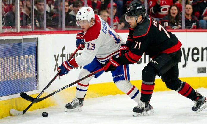 canadiens-hurricanes-game-2-playoffs-2026 A dynamic action photograph from the 2026 NHL Eastern Conference Finals Game 1, capturing Montreal Canadiens forward Cole Caufield fighting off Carolina Hurricanes forward Taylor Hall for possession of the hockey puck during intense, physical board play at Lenovo Center.