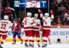 Carolina Hurricanes and Montreal Canadiens Game 4 Recap & Score A group of Carolina Hurricanes players in white away jerseys, including Sebastian Aho (20) and Jordan Staal (11), huddle on the ice in triumph, celebrating a first-period goal against the Montreal Canadiens during Game 4 of the Eastern Conference Final. In the background, a large Jumbotron confirms the event and period.