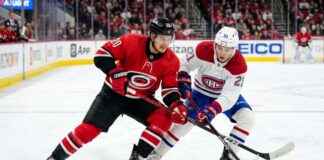 How to Watch Carolina Hurricanes vs Montreal Canadiens Game 4 Today Carolina Hurricanes’ Sebastian Aho (jersey 20) and Montreal Canadiens’ Lane Hutson (jersey 21) battle intensely for a hockey puck on the ice during Game 4 of the 2026 Eastern Conference Final. Both players are low to the ice, locking sticks over the puck, with a crowded arena and hockey boards visible in the background.