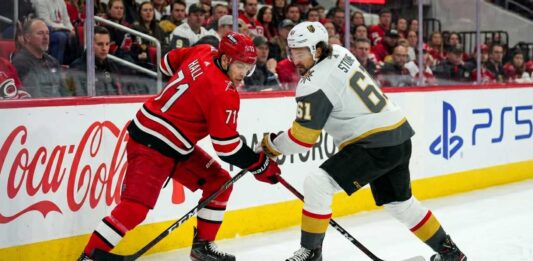 Carolina Hurricanes forward Taylor Hall takes a face-off against Vegas Golden Knights captain Mark Stone during the Stanley Cup Final, with Coca-Cola and PS5 ads visible on the boards.