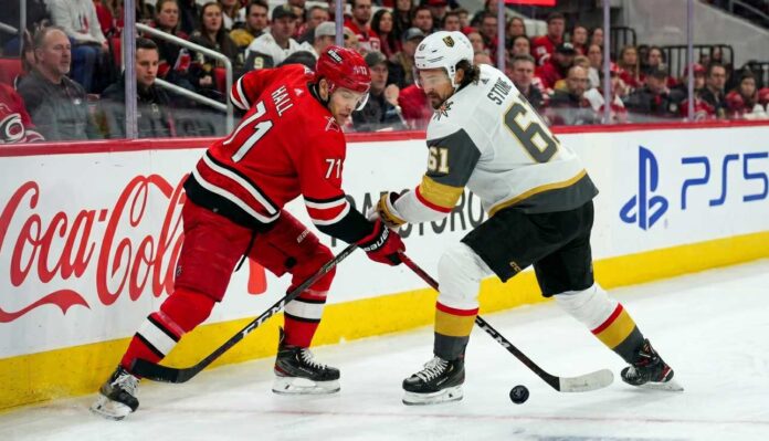 Carolina Hurricanes forward Taylor Hall takes a face-off against Vegas Golden Knights captain Mark Stone during the Stanley Cup Final, with Coca-Cola and PS5 ads visible on the boards.