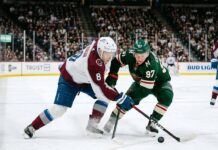 Intense puck battle between Colorado Avalanche defenseman Cale Makar (#8) and Minnesota Wild forward Kirill Kaprizov (#97) during an NHL playoff game at Xcel Energy Center.