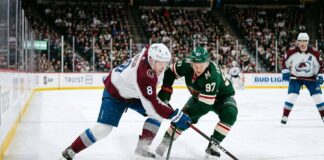 Intense puck battle between Colorado Avalanche defenseman Cale Makar (#8) and Minnesota Wild forward Kirill Kaprizov (#97) during an NHL playoff game at Xcel Energy Center.