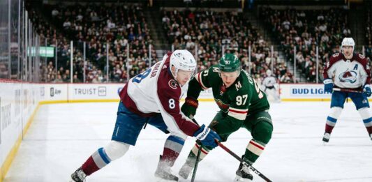 Intense puck battle between Colorado Avalanche defenseman Cale Makar (#8) and Minnesota Wild forward Kirill Kaprizov (#97) during an NHL playoff game at Xcel Energy Center.