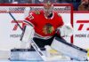 Chicago Blackhawks Trade Rumors: Connor Hellebuyck & Winnipeg Jets A photorealistic image showing goalie Connor Hellebuyck in a red Chicago Blackhawks home uniform and custom Blackhawks mask in the goal crease, illustrating potential trade rumors from the Winnipeg Jets.