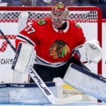 Chicago Blackhawks Trade Rumors: Connor Hellebuyck & Winnipeg Jets A photorealistic image showing goalie Connor Hellebuyck in a red Chicago Blackhawks home uniform and custom Blackhawks mask in the goal crease, illustrating potential trade rumors from the Winnipeg Jets.