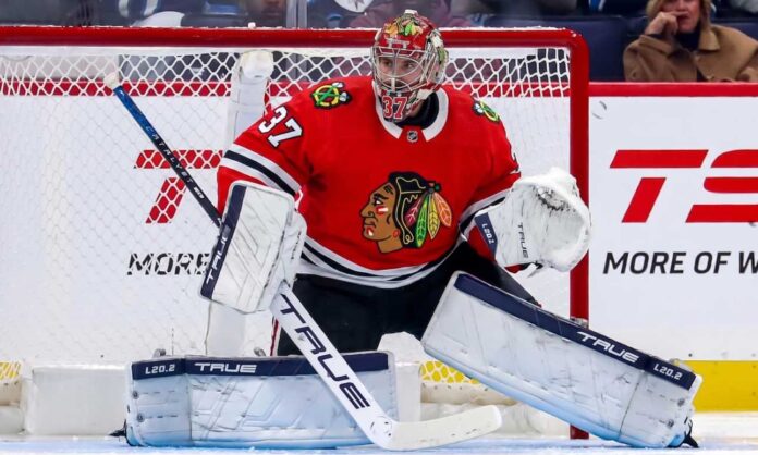 connor-hellebuyck-chicago-blackhawks-trade-rumors-winnipeg-jets A photorealistic image showing goalie Connor Hellebuyck in a red Chicago Blackhawks home uniform and custom Blackhawks mask in the goal crease, illustrating potential trade rumors from the Winnipeg Jets.