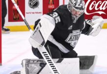 Los Angeles Kings goalie Darcy Kuemper in his black Kings jersey with number 35, making a stick save on the ice. This image relates to current NHL trade rumors concerning Kuemper's future with LA.