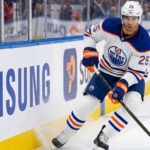 Darnell Nurse Trade Rumors: Will the Edmonton Oilers Move Him? Edmonton Oilers defenseman Darnell Nurse (#25) in away white jersey skating along the boards with the puck, amid offseason trade rumors.