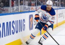 Edmonton Oilers defenseman Darnell Nurse (#25) in away white jersey skating along the boards with the puck, amid offseason trade rumors.