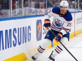 Darnell Nurse Trade Rumors: Will the Edmonton Oilers Move Him? Edmonton Oilers defenseman Darnell Nurse (#25) in away white jersey skating along the boards with the puck, amid offseason trade rumors.
