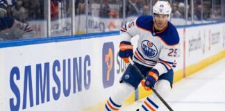 Edmonton Oilers defenseman Darnell Nurse (#25) in away white jersey skating along the boards with the puck, amid offseason trade rumors.