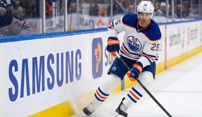 darnell-nurse-edmonton-oilers-trade-rumors Edmonton Oilers defenseman Darnell Nurse (#25) in away white jersey skating along the boards with the puck, amid offseason trade rumors.