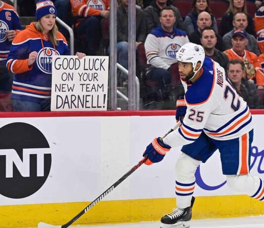 Edmonton Oilers defenseman Darnell Nurse skating on the ice with a fan sign in the background reading 'GOOD LUCK ON YOUR NEW TEAM DARNELL!' during intense offseason trade rumors.