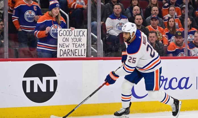 Edmonton Oilers defenseman Darnell Nurse skating on the ice with a fan sign in the background reading 'GOOD LUCK ON YOUR NEW TEAM DARNELL!' during intense offseason trade rumors.