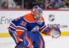 A conceptual photograph visualizing goaltender Filip Gustavsson wearing a royal blue and orange Edmonton Oilers uniform with number 32, representing the rumored NHL trade from the Minnesota Wild.
