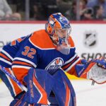 A conceptual photograph visualizing goaltender Filip Gustavsson wearing a royal blue and orange Edmonton Oilers uniform with number 32, representing the rumored NHL trade from the Minnesota Wild.